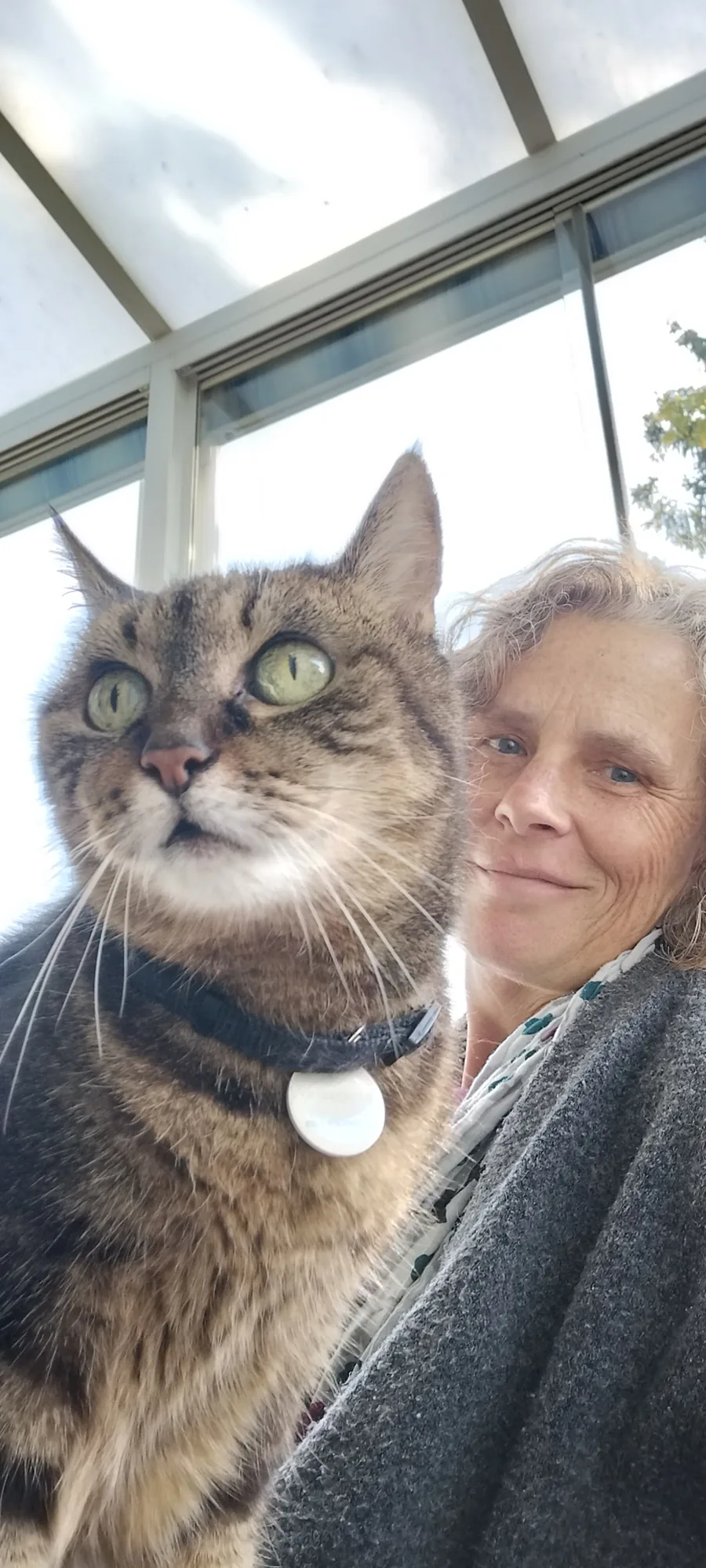 Sandra sitzt mit einer grossen getigerten Katze auf dem Arm im Wintergarten