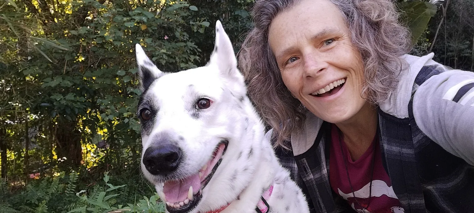 Sandra lacht in die Kamera, dicht neben ihr sitzt ihr weisser Hund Dancer